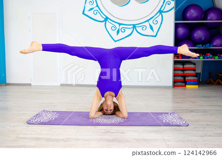Woman performing a headstand split yoga pose in a studio 124142966