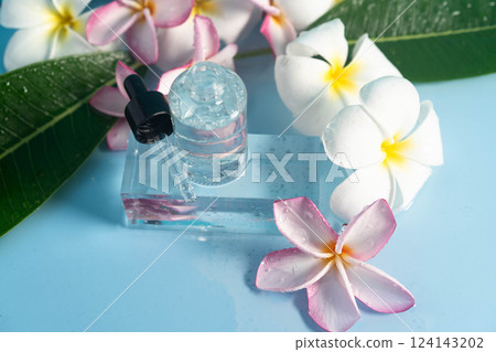 A pretty blue setting features a serum bottle beside lovely plumeria flowers for hydration. 124143202