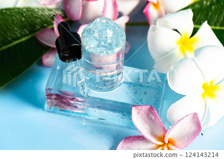 Clear serum in a dropper bottle rests on a blue surface with vibrant frangipani flowers and leaves. Clear serum in a dropper bottle rests on a blue surface with vibrant frangipani flowers and leaves. 124143214