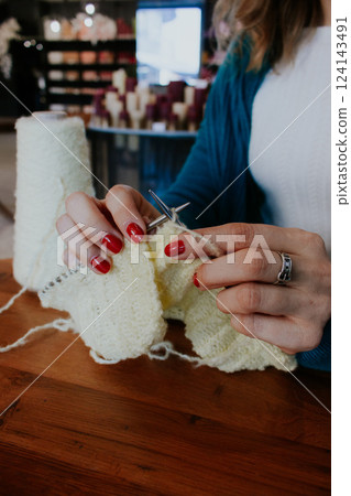 Women hands holding knitting needles and yellow cotton knitted work. Knitting woman with bobbins of yarn and yellow knitwear. Needlework in process. Knitting hobby. Knitter work.  124143491