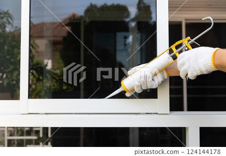 Construction worker using silicone sealant caulk for repair leaked inside window frame. 124144178