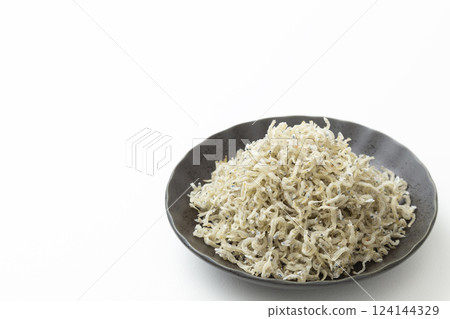 Dried small sardines served on a black plate on a white background Dried small sardines served on a black plate on a white background 124144329