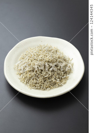 Dried small sardines served on a plate on a black background Dried small sardines served on a plate on a black background 124144345