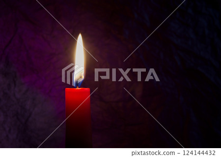 Red candle with flickering flame against a textured dark background 124144432