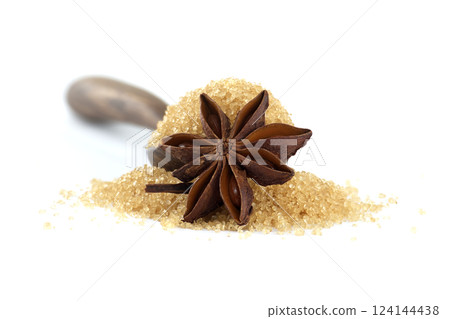 Aromatic star anise rests atop a spoonful of natural raw cane sugar on a seamless white backdrop. 124144438