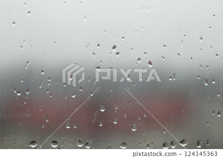 A close-up image of raindrops on a window, with the water droplets visibly clinging to the glass. The background could feature a blurred outdoor scene 124145363