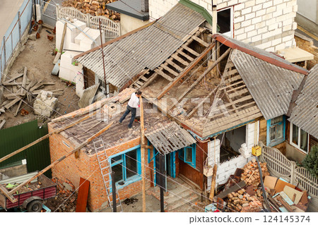 An old, dilapidated house with a worn-out wooden roof, showing signs of renovation. The exterior of the building is in ruins, with traces of war damage An old, dilapidated house with a worn-out wooden roof, showing signs of renovation. The exterior of the building is in ruins, with traces of war damage 124145374