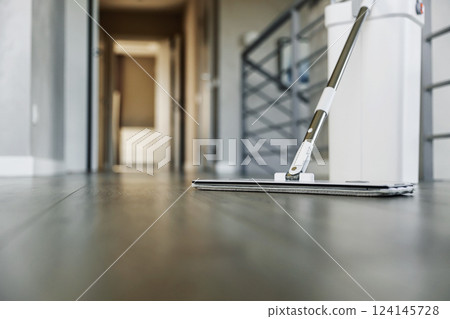 Cleaning supplies: mop and bucket with wringer sitting on wooden laminate floor in modern corridor, wet equipment tools, housekeeping concept. Emphasizing home sanitation, cleanliness, hygiene Cleaning supplies: mop and bucket with wringer sitting on wooden laminate floor in modern corridor, wet equipment tools, housekeeping concept. Emphasizing home sanitation, cleanliness, hygiene 124145728