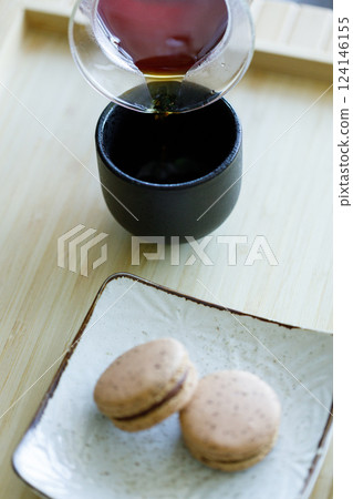 Black coffee pouring into cup and black tea flavor macaron on wooden background. Black coffee pouring into cup and black tea flavor macaron on wooden background. 124146155