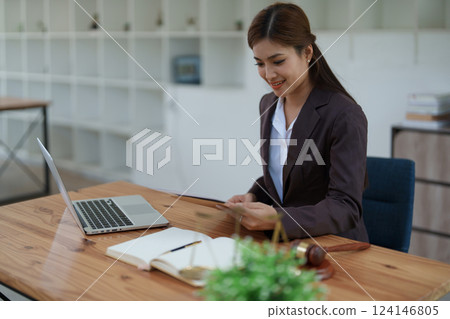 female attorney advisor at a law firm reviews legal documents at her desk equipped with a laptop notebook and scales of justice in the office female attorney advisor at a law firm reviews legal documents at her desk equipped with a laptop notebook and scales of justice in the office 124146805
