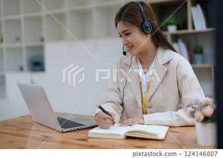 Asian businesswoman wears a headset while participation in an online video conference discussing marketing and finance strategies effectively Asian businesswoman wears a headset while participation in an online video conference discussing marketing and finance strategies effectively 124146807