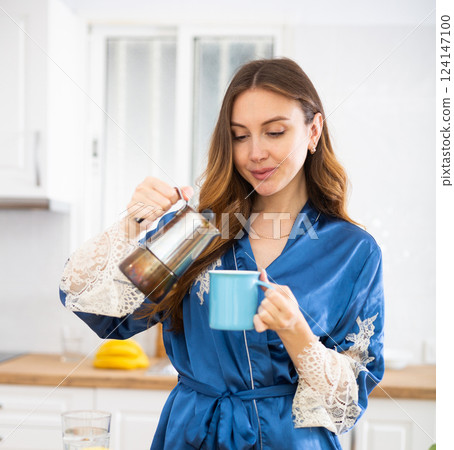 Woman in housecoat making coffee in kitchen 124147100