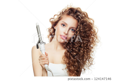 Successful brown haired woman with shiny long curly hairstyle showing curling iron. 124147146