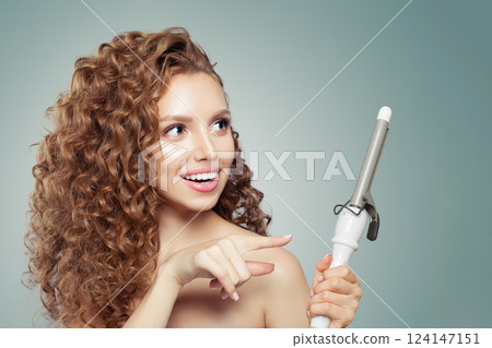 Studio portrait of brunette model using curling iron on grey background.  124147151