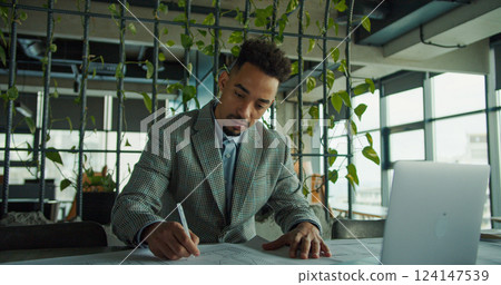 Businessman writing on documents in modern workspace Businessman writing on documents in modern workspace 124147539