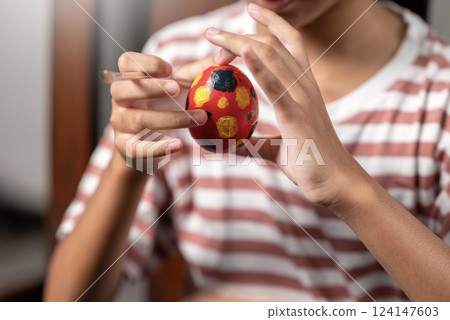 Indonesian southeast asian little girl is painting on an egg with a paintbrush for easter egg decoration on the table. Concept of celebrating the easter holiday 124147603