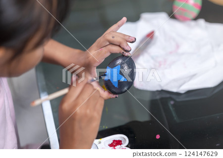 Indonesian southeast asian little girl is painting on an egg with a paintbrush for easter egg decoration on the table. Concept of celebrating the easter holiday Indonesian southeast asian little girl is painting on an egg with a paintbrush for easter egg decoration on the table. Concept of celebrating the easter holiday 124147629