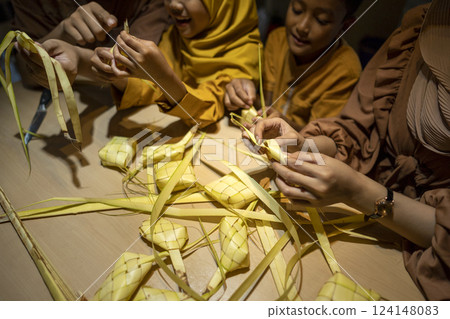 Indonesian Muslim family weaving ketupat rice dumpling from young coconut leaves. Traditional Muslim food during celebration of Happy Lebaran, Eid Al Fitr, Idul Fitri, and Ramadan Mubarak celebration 124148083