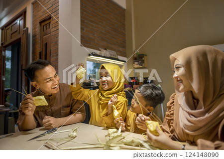 Indonesian Muslim family weaving ketupat rice dumpling from young coconut leaves. Traditional Muslim food during celebration of Happy Lebaran, Eid Al Fitr, Idul Fitri, and Ramadan Mubarak celebration 124148090