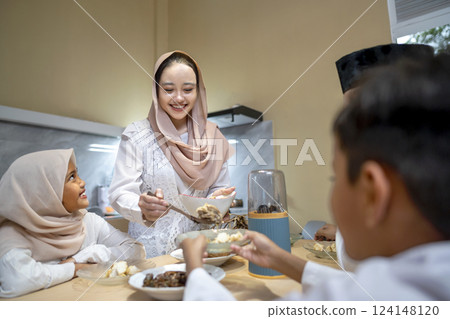 Indonesian Muslim wife serving ketupat rice dumpling for family in the house. Traditional Muslim food during the celebration of Happy Lebaran, Eid Al Fitr, Idul Fitri, and Ramadan Mubarak celebration Indonesian Muslim wife serving ketupat rice dumpling for family in the house. Traditional Muslim food during the celebration of Happy Lebaran, Eid Al Fitr, Idul Fitri, and Ramadan Mubarak celebration 124148120
