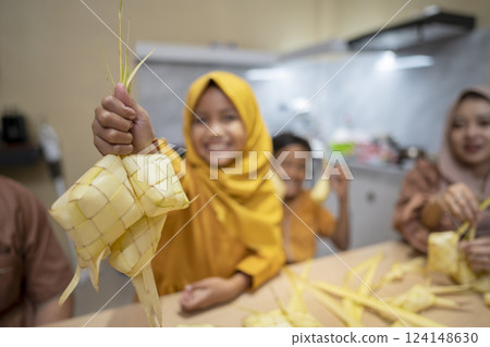 Indonesian Muslim family weaving ketupat rice dumpling from young coconut leaves. Traditional Muslim food during celebration of Happy Lebaran, Eid Al Fitr, Idul Fitri, and Ramadan Mubarak celebration 124148630