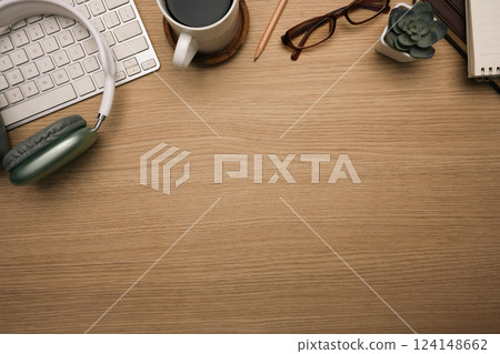 Top view shot of wooden desk with headphone, keyboard, a cup of coffee and eyeglasses 124148662