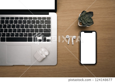 Top view of smartphone with blank screen, laptop and wireless earbuds wooden desk 124148677