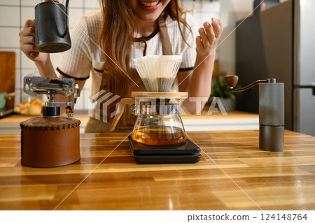 Happy young woman wearing apron preparing a fresh pour over coffee in stylish kitchen 124148764