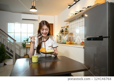 Beautiful young woman enjoying a delicious breakfast in a cozy home kitchen 124148768