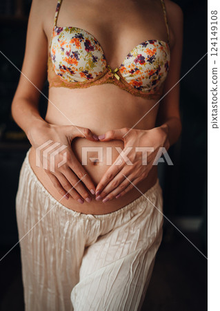Pregnant young woman creating heart shape with hands on her belly 124149108