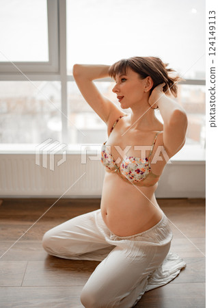 Young pregnant woman posing gracefully indoors near large windows 124149113