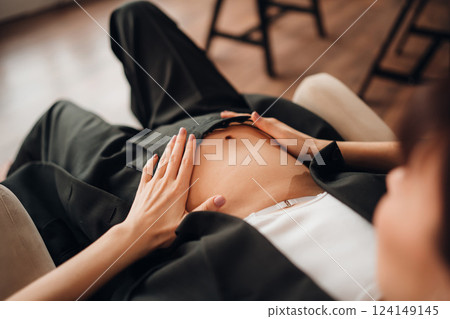 Young pregnant woman gently touching her belly while relaxing at home Young pregnant woman gently touching her belly while relaxing at home 124149145