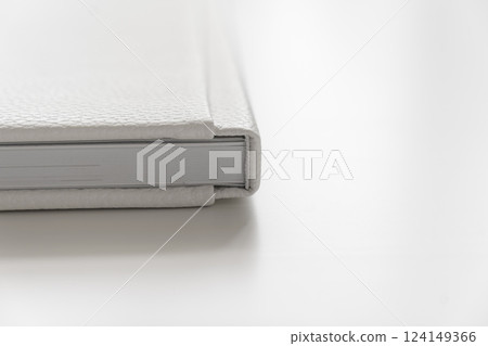 corner of book in white leather cover on white table. binding for photo album 124149366