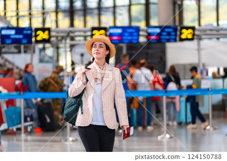 Caucasian happy young woman in straw hat holds passport with boarding pass. Defocused check flight area in background. The concept of vacation and flight trip Caucasian happy young woman in straw hat holds passport with boarding pass. Defocused check flight area in background. The concept of vacation and flight trip 124150788