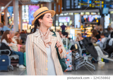 Mid shot of Caucasian young woman in a jacket smiling and looking to the right side. Blurred departure lounge in the background. Copy space. Concept of travel 124150802