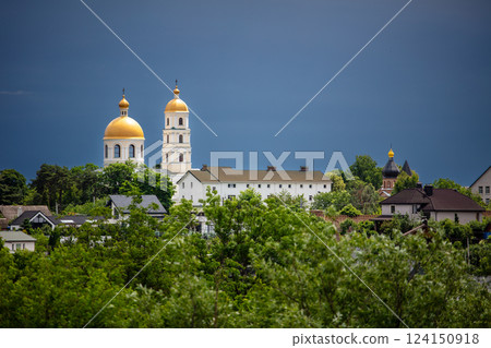 A picturesque town lush greenery, and golden-domed churches in the background. The dramatic sky adds contrast, creating a serene yet moody atmosphere. 124150918