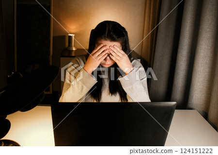Woman working on computer late evening at home office. Concentrated female freelancer trying to solve business problems. Working and suffering from weariness. 124151222
