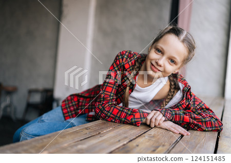 Portrait of happy preteen girl with braided hair wearing red plaid shirt, leaning comfortably on wooden windowsill by window, enjoying leisure time in cozy indoor room, smiling looking at camera Portrait of happy preteen girl with braided hair wearing red plaid shirt, leaning comfortably on wooden windowsill by window, enjoying leisure time in cozy indoor room, smiling looking at camera 124151485