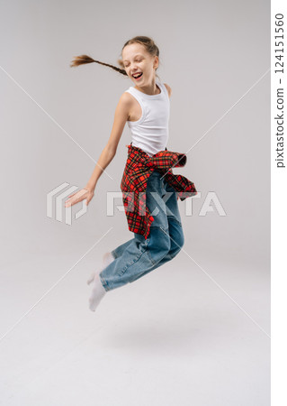 Studio portrait of energetic preteen girl jumping mid-air, radiating happiness and freedom with playful smile and dynamic pose, embodying spirit of childhood joy. Concept of carefree preadolescence. Studio portrait of energetic preteen girl jumping mid-air, radiating happiness and freedom with playful smile and dynamic pose, embodying spirit of childhood joy. Concept of carefree preadolescence. 124151560