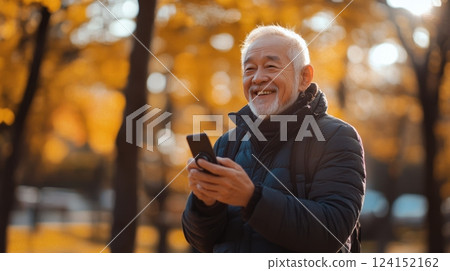 Happy elderly man chatting with family online, autumn leaves and soft sunlight. Using phone stabilizer 124152162
