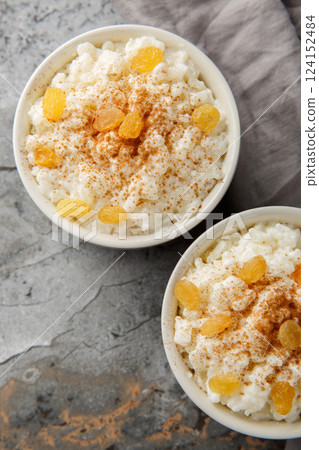 Creamy Rice Pudding with milk and sugar, then finish with cinnamon, vanilla and raisins closeup on the bowl. Vertical top view Creamy Rice Pudding with milk and sugar, then finish with cinnamon, vanilla and raisins closeup on the bowl. Vertical top view 124152484