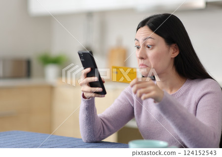 Perplexed asian woman paying online in the kitchen 124152543