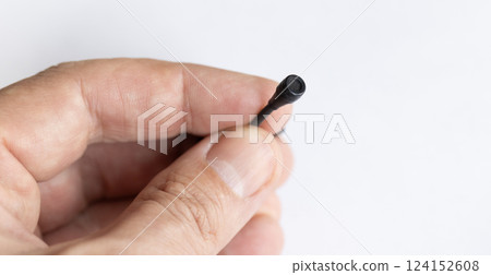 A close-up of a hand holding a small black wired microphone against a white background. The tiny microphone has a thin cable and a mesh-covered tip, designed for discreet audio recording. A close-up of a hand holding a small black wired microphone against a white background. The tiny microphone has a thin cable and a mesh-covered tip, designed for discreet audio recording. 124152608