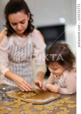 Happy family mother and little child daughter cutting cookies of raw gingerbread dough in kitchen. Christmas traditions 124152772