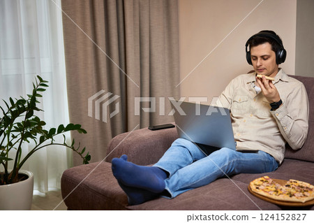 man sitting on sofa and eating pizza while working on laptop 124152827