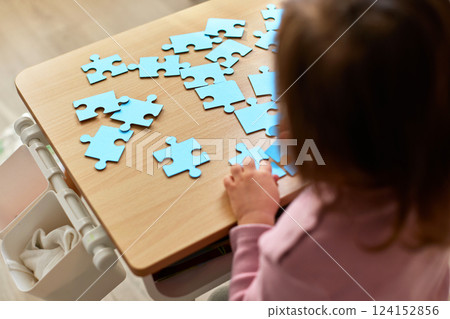 Cute little child girl connecting puzzle pieces on wooden desk in room, top view Cute little child girl connecting puzzle pieces on wooden desk in room, top view 124152856