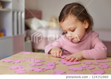 Cute little child girl connecting puzzle pieces on wooden desk in room, Education concept. Cute little child girl connecting puzzle pieces on wooden desk in room, Education concept. 124152860