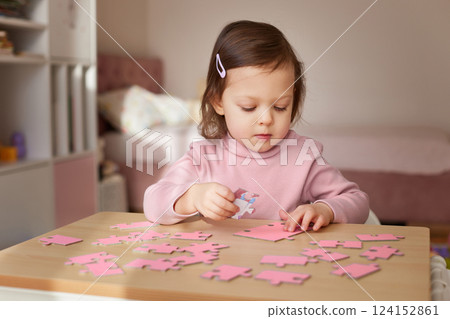 Cute little child girl connecting puzzle pieces on wooden desk in room Cute little child girl connecting puzzle pieces on wooden desk in room 124152861