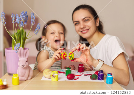 Happy mother and cute little child girl showing painted Easter egg and having fun at home. Mom and daughter painting eggs before Easter together. Easter Family traditions Happy mother and cute little child girl showing painted Easter egg and having fun at home. Mom and daughter painting eggs before Easter together. Easter Family traditions 124152883