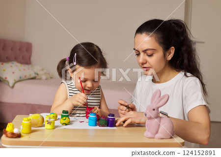 Happy mother and cute little child girl are preparing to celebrate Easter at home. Mom and daughter painting eggs before Easter together. Happy mother and cute little child girl are preparing to celebrate Easter at home. Mom and daughter painting eggs before Easter together. 124152891